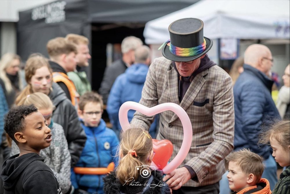 Lange Jan met hoge hoed maakt een ballonhart, omringd door kinderen