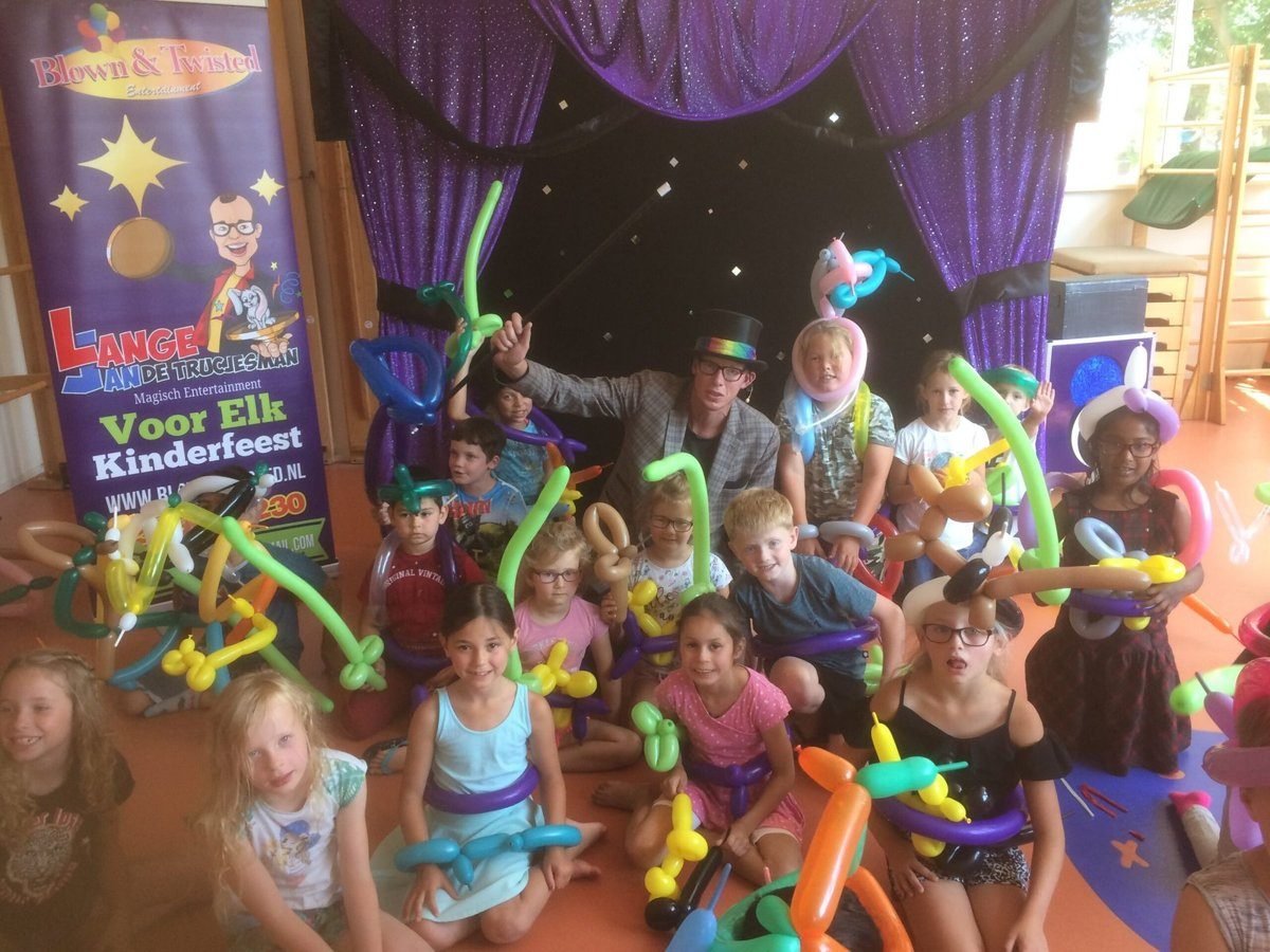Lange Jan met hoge hoed voor het podium, omringd door kinderen met ballonfiguren